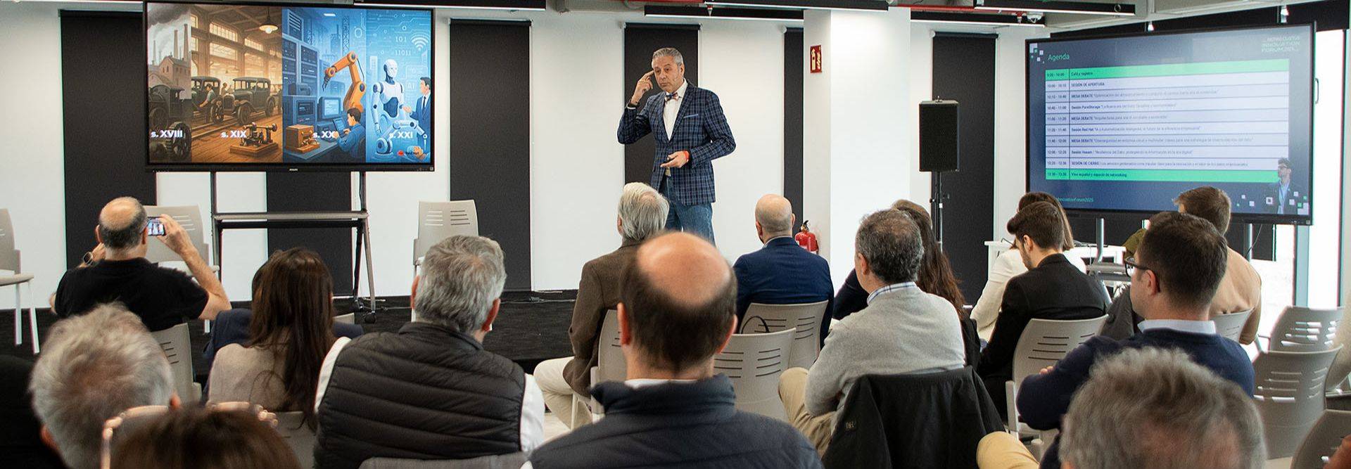 Un ponente habla frente a un público en un evento sobre tecnología, mientras muestra imágenes en pantallas.
