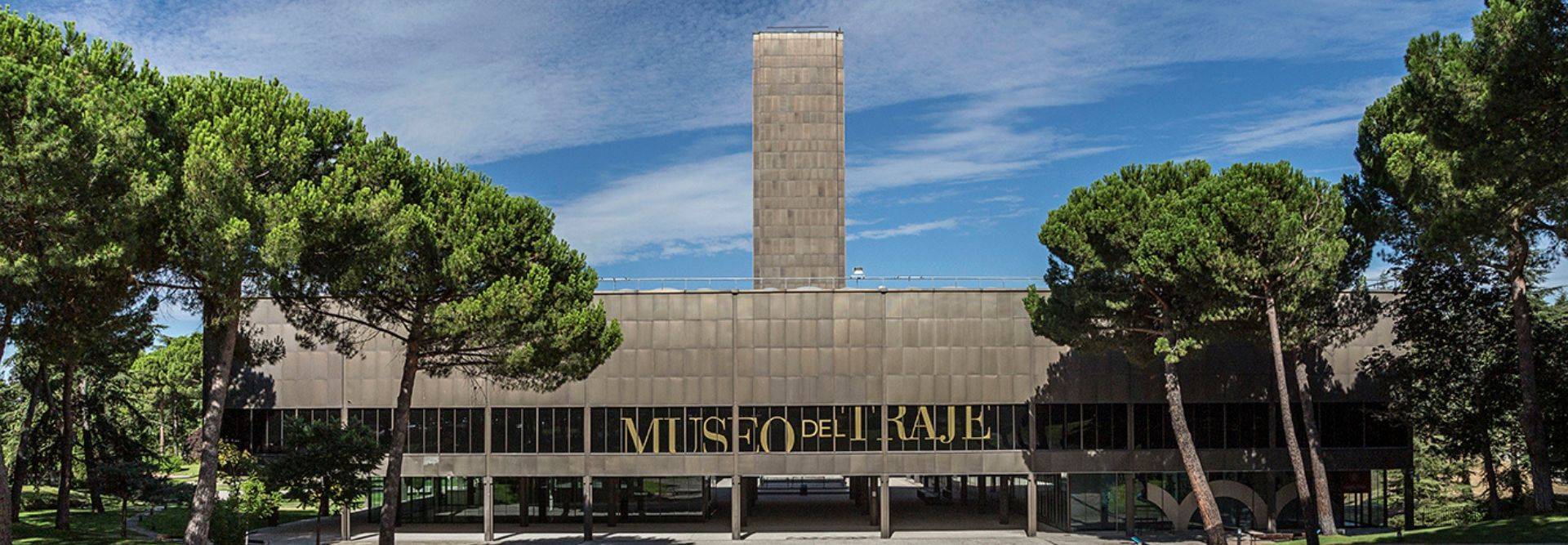 Edificio moderno del Museo del Traje rodeado de árboles y con un cielo despejado.