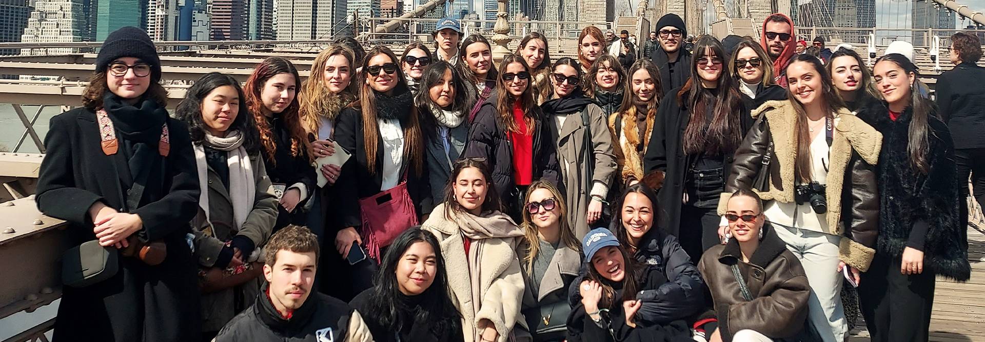 Un grupo numeroso de estudiantes sonrientes posando en un puente con un fondo urbano.