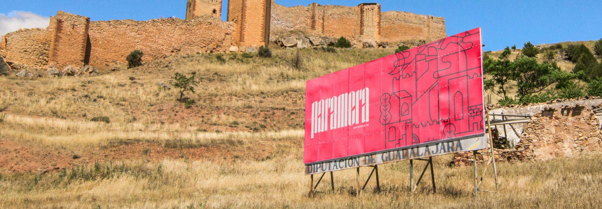 Un cartel colorido se encuentra en primer plano frente a un castillo en una colina.