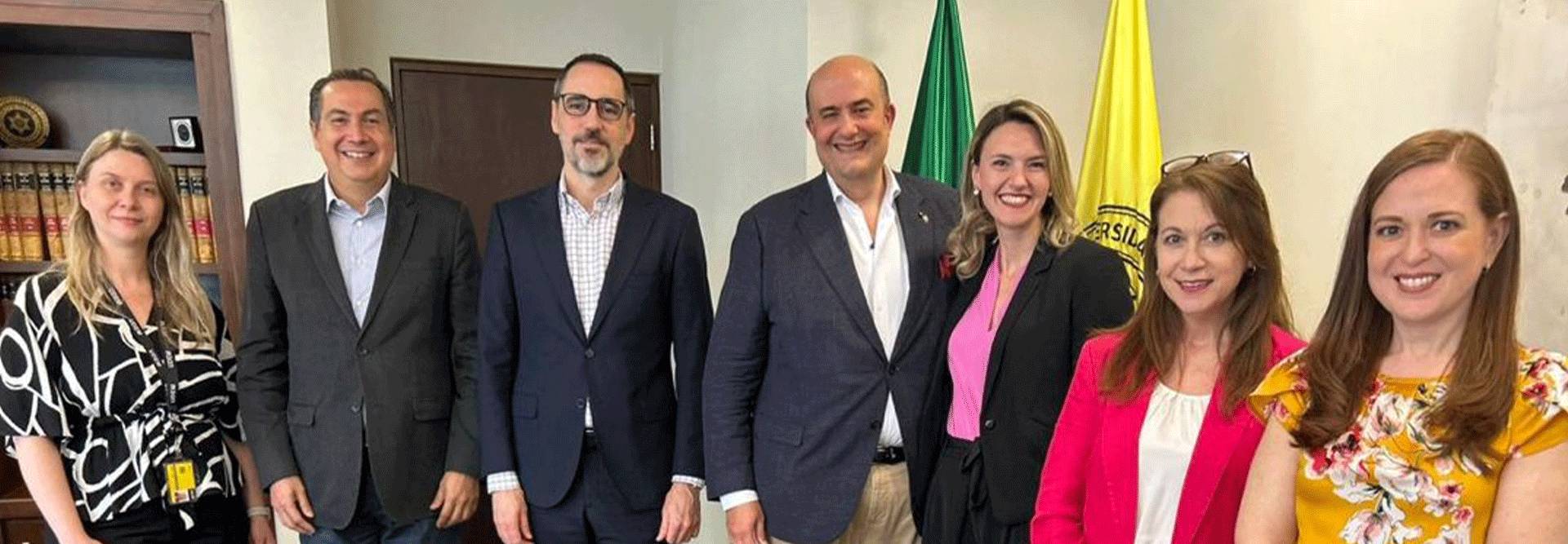 Un grupo de personas sonrientes posando en un ambiente formal con banderas de fondo.