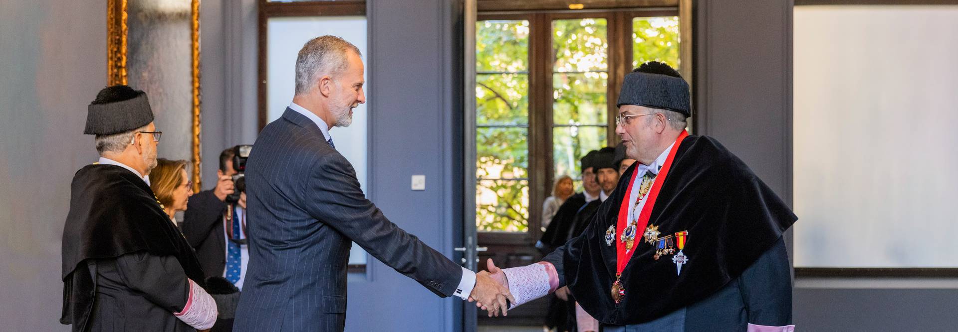 Una ceremonia donde se lleva a cabo un saludo formal entre dos personas en un ambiente académico.