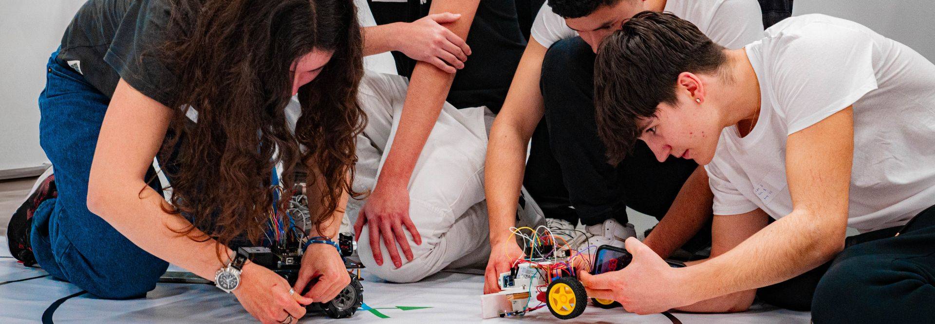 Un grupo de estudiantes trabaja en un proyecto de robótica, ajustando un pequeño robot en una superficie blanca.