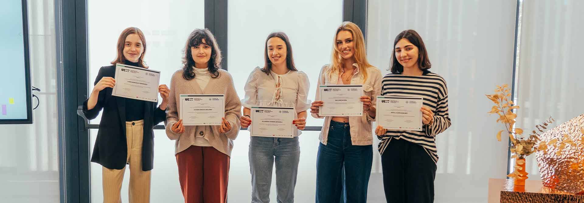 Un grupo de cinco mujeres sostiene certificados en un evento de entrega de premios.