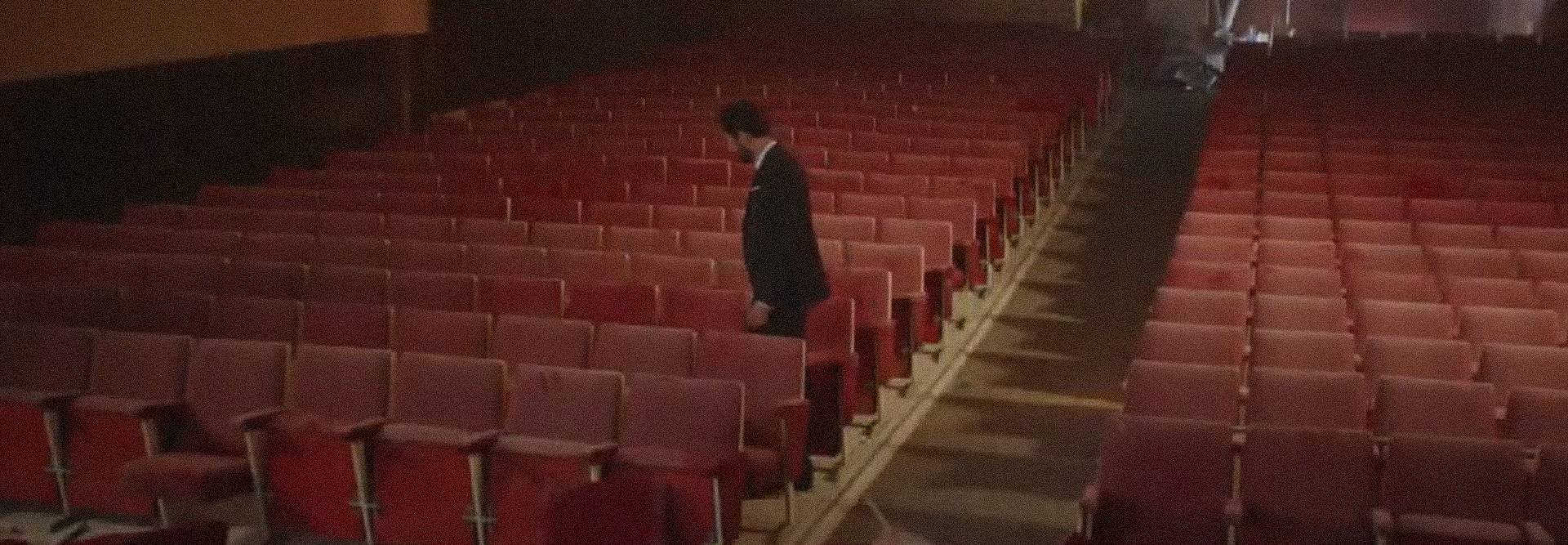 Un hombre camina solo entre las filas vacías de asientos en un teatro.