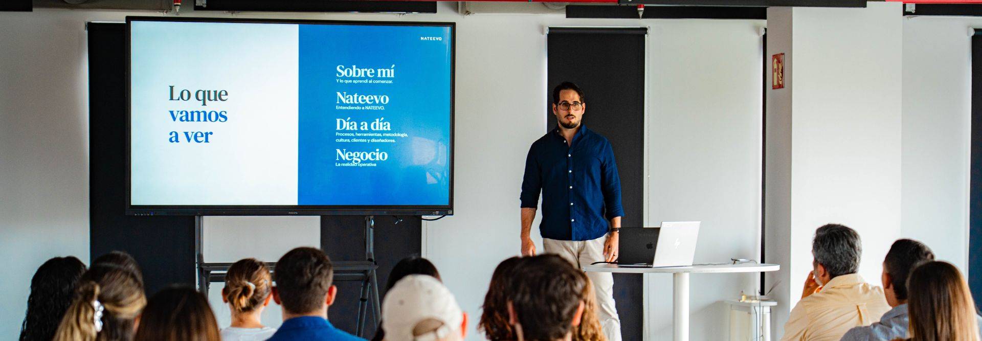Un presentador expone un tema frente a una audiencia en un espacio moderno.