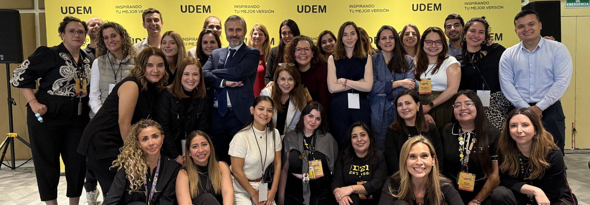 Grupo de personas posando frente a un fondo amarillo con el logo de UDEM.