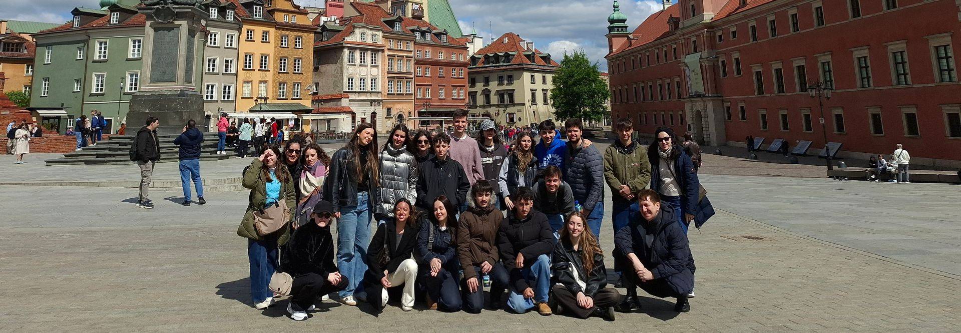 Un grupo grande de personas posando en una plaza con edificios coloridos de fondo.