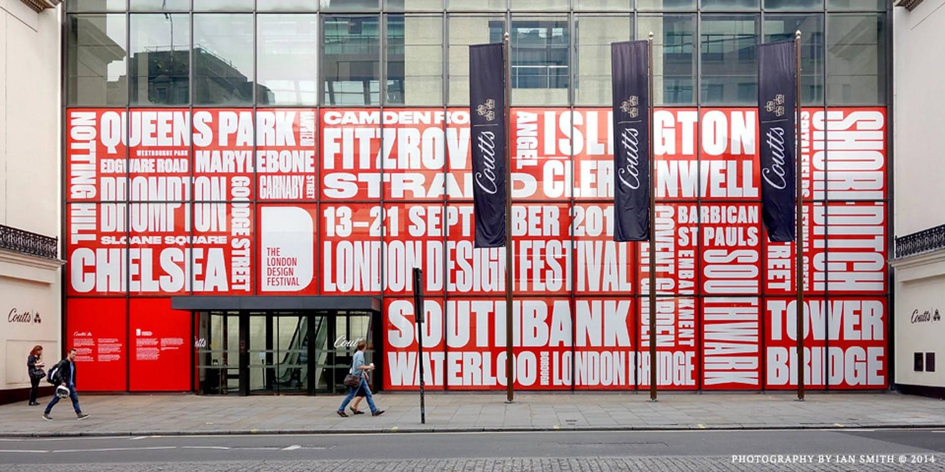 Una fachada de edificio con un gran mural de texto rojo que muestra nombres de lugares y eventos en Londres.