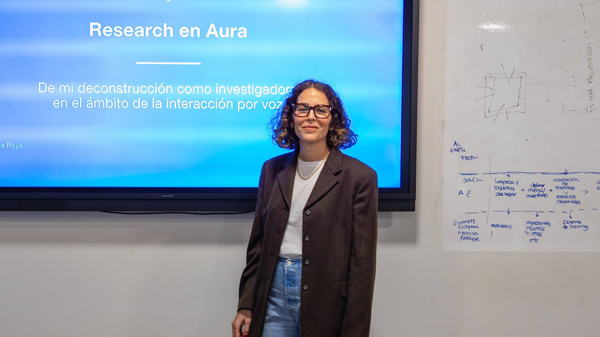 Una persona se presenta frente a una pantalla que muestra un título y un texto sobre investigación.