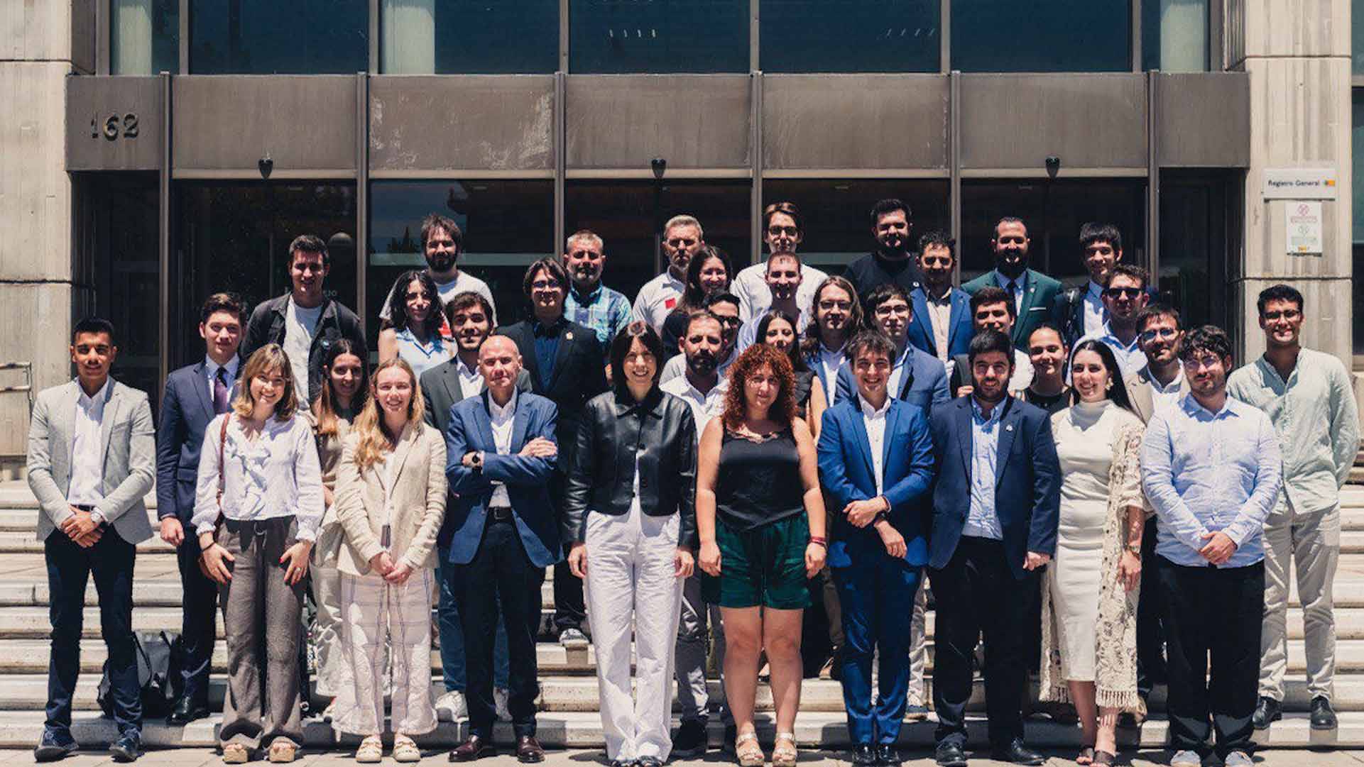 Un grupo grande de personas posando frente a un edificio durante un día soleado.