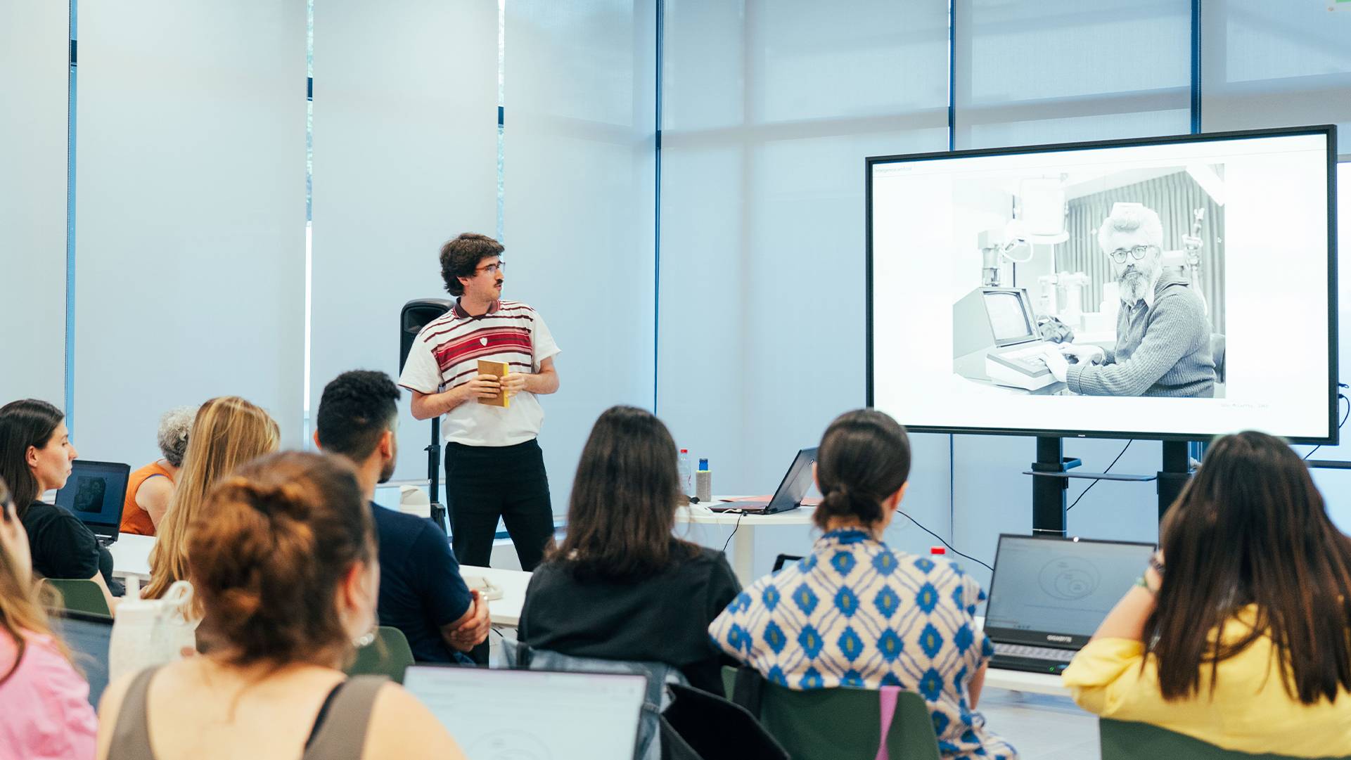 Un presentador expone ante un público en una sala con pantallas de proyección.
