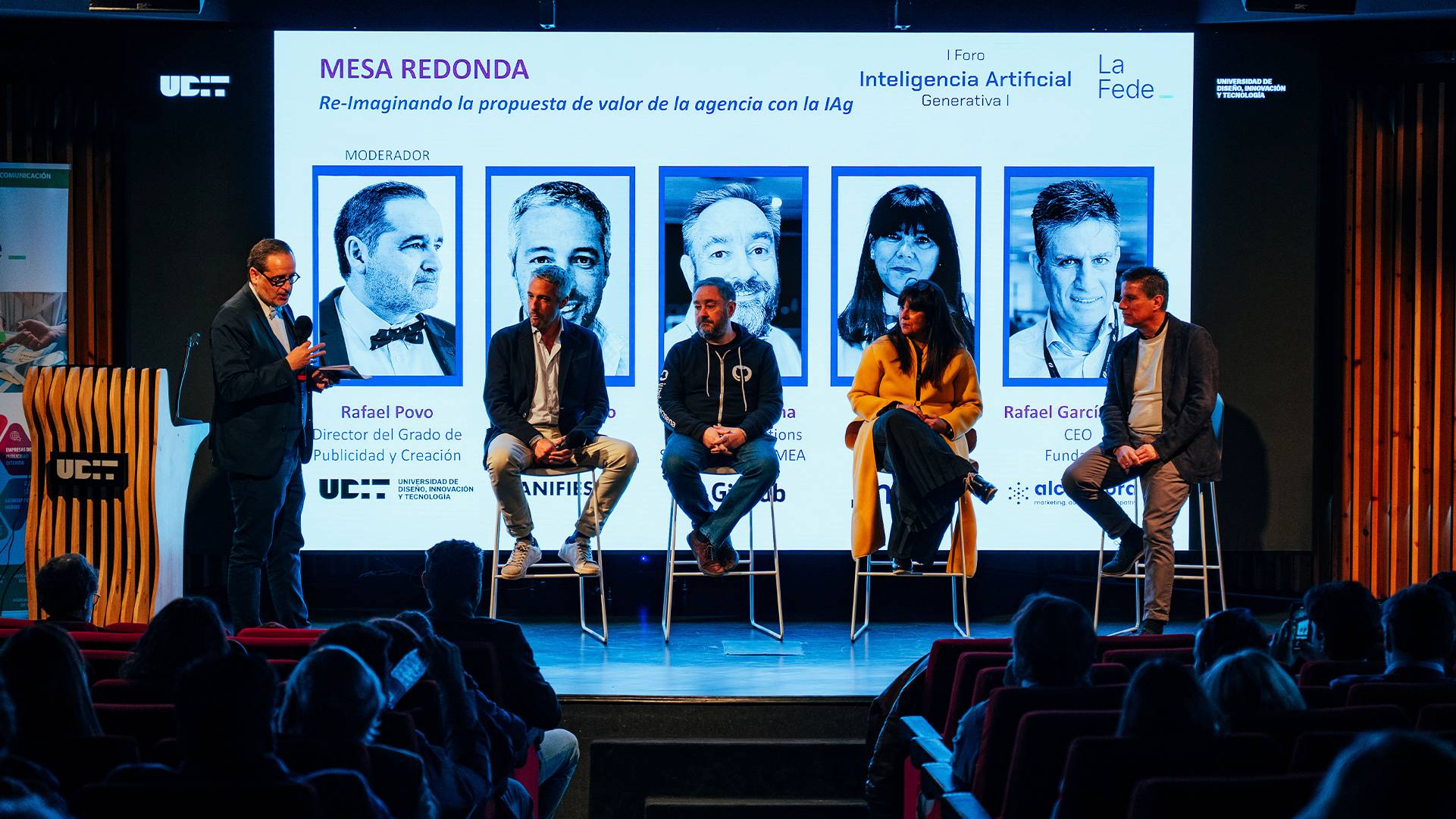 Un panel de discusión sobre inteligencia artificial con varios ponentes y un moderador en el escenario.