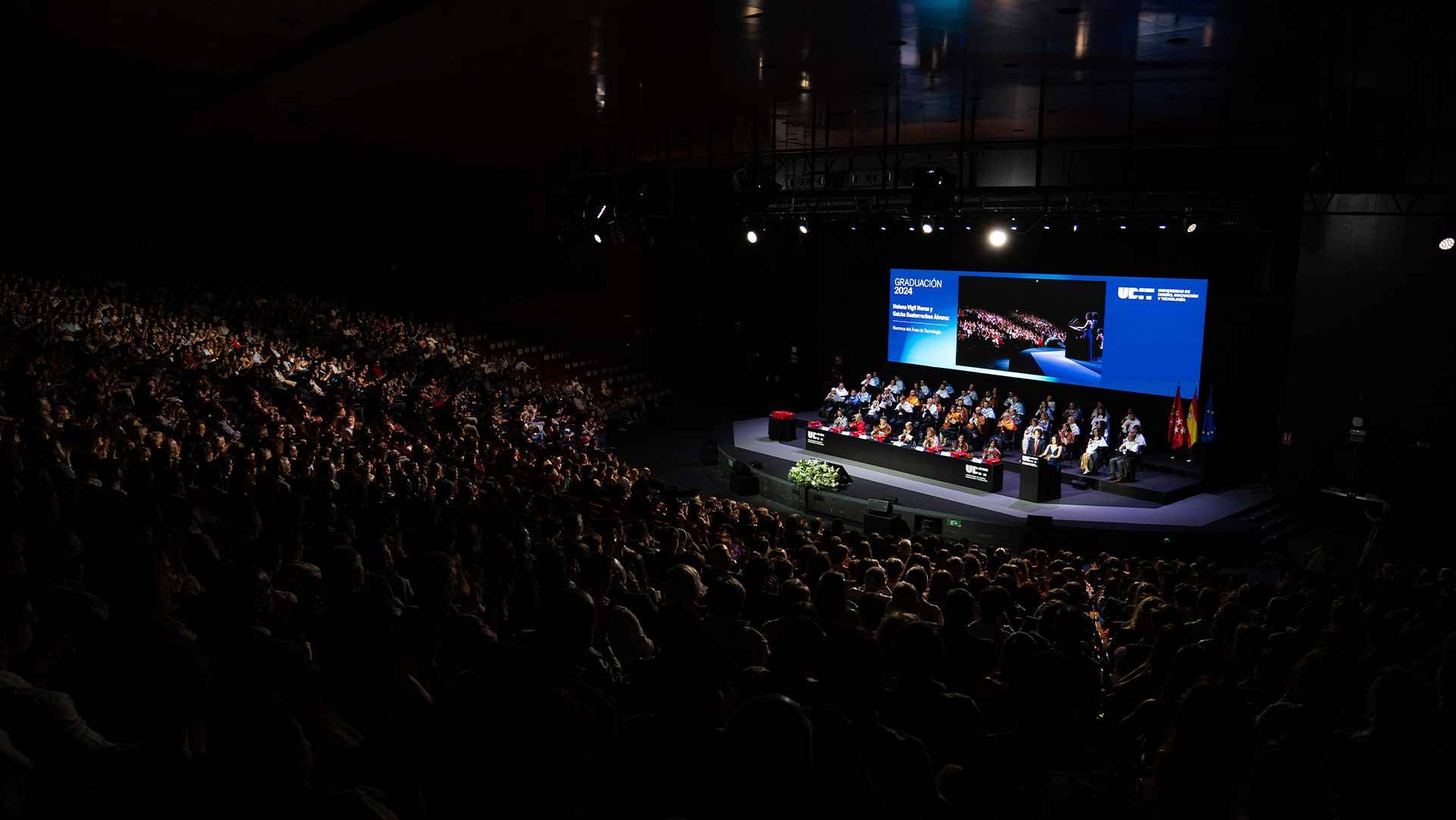 Un evento con un gran público asistente y un grupo de personas en el escenario.
