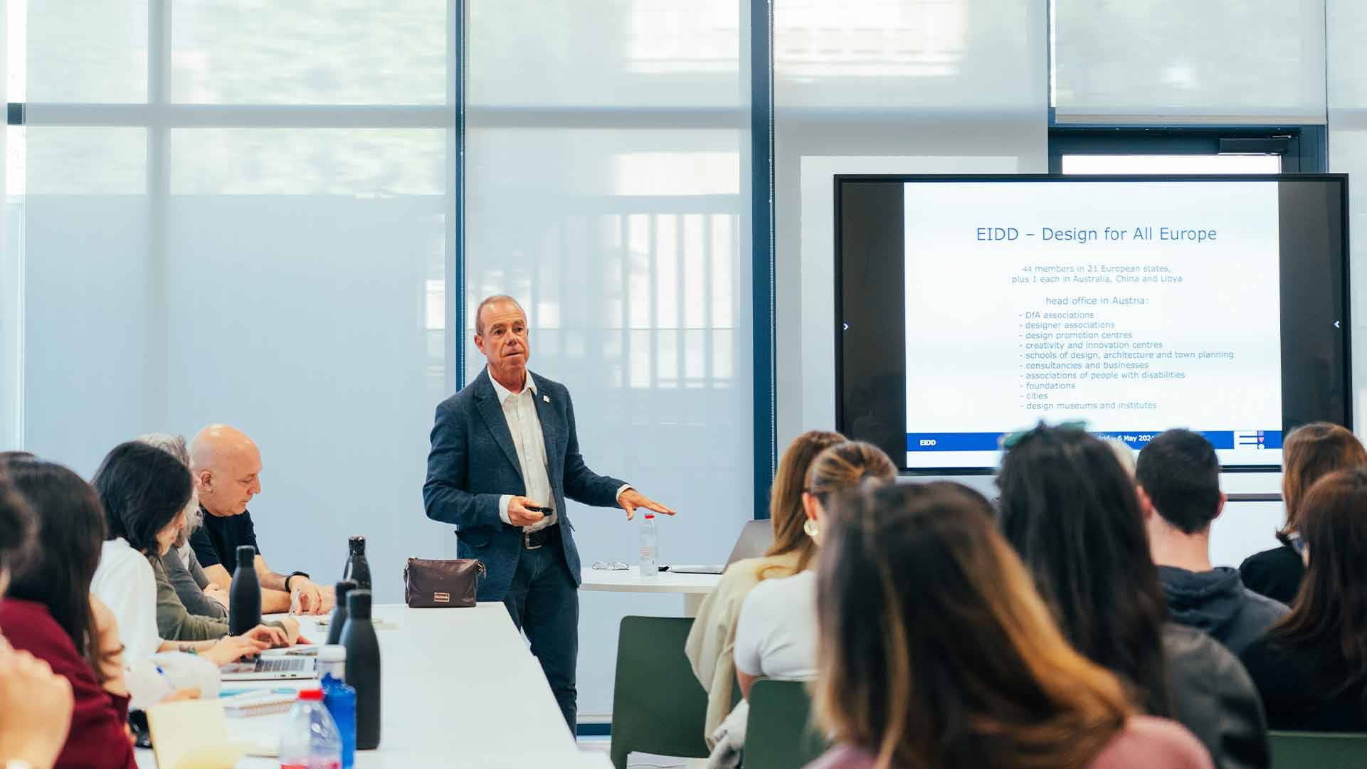 Un profesor está presentando una clase frente a un grupo de estudiantes en un aula moderna.