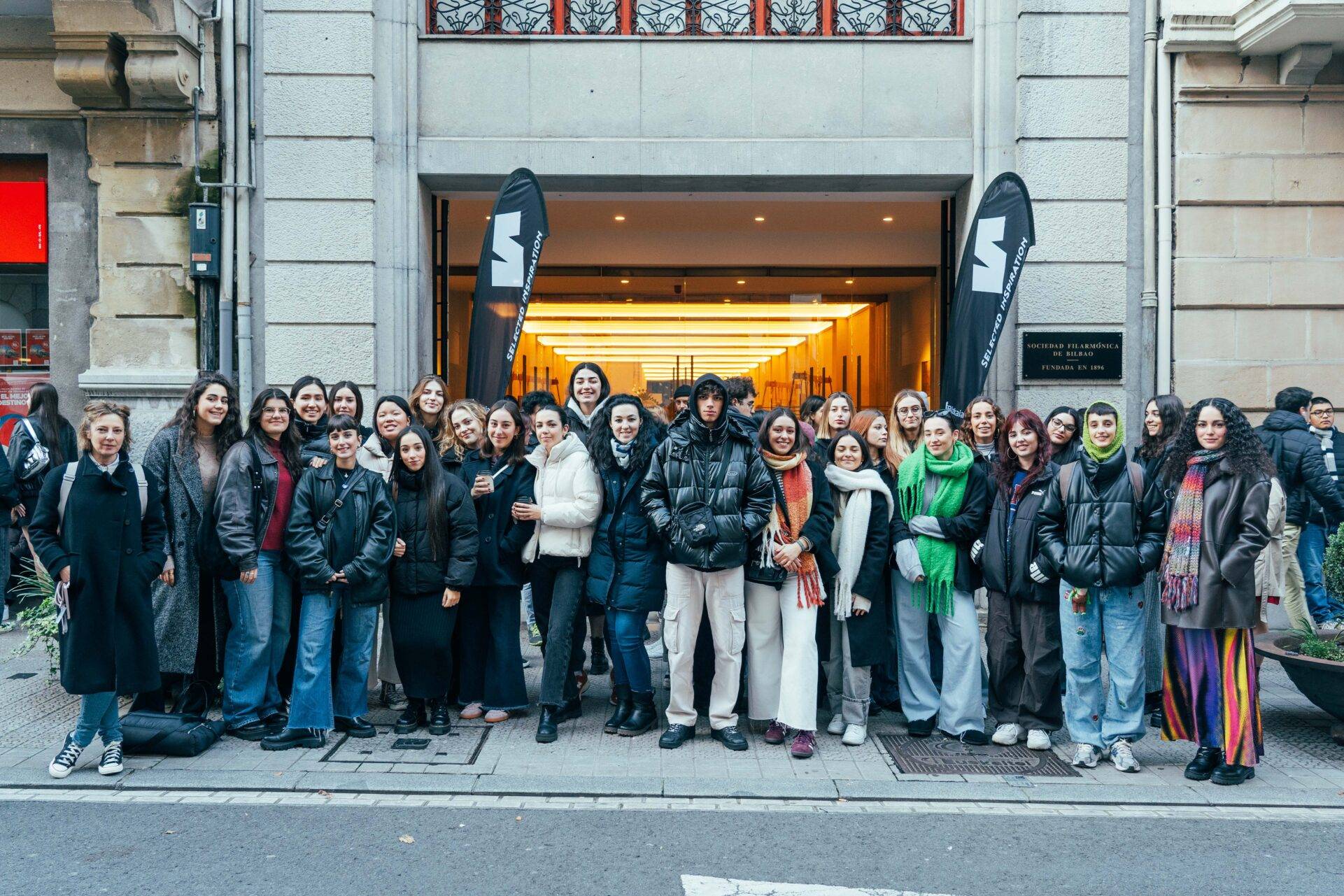 Un grupo grande de personas posando juntas frente a un edificio con banderas.