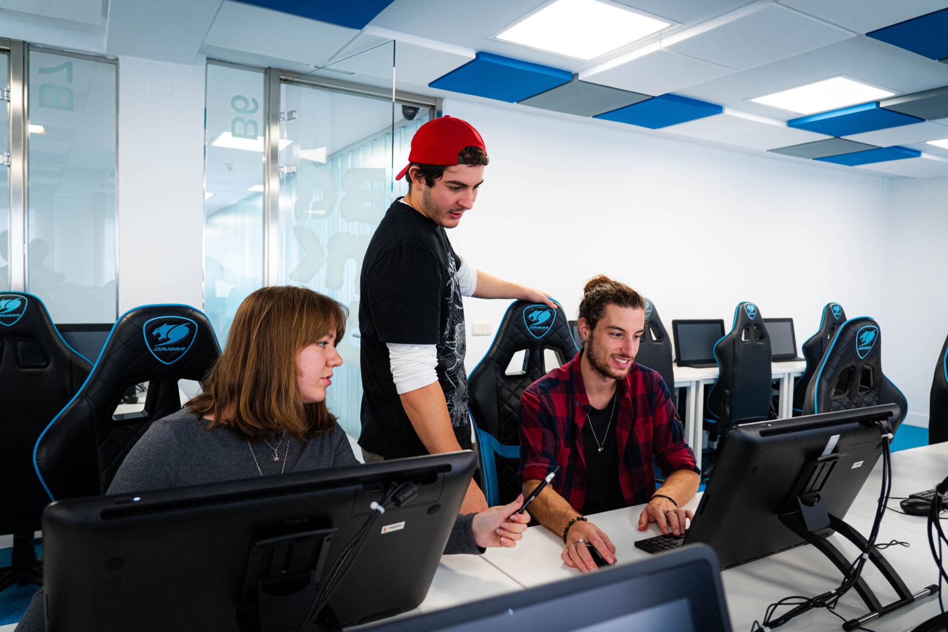 Un grupo de tres jóvenes colaborando en un entorno de trabajo moderno frente a computadoras.