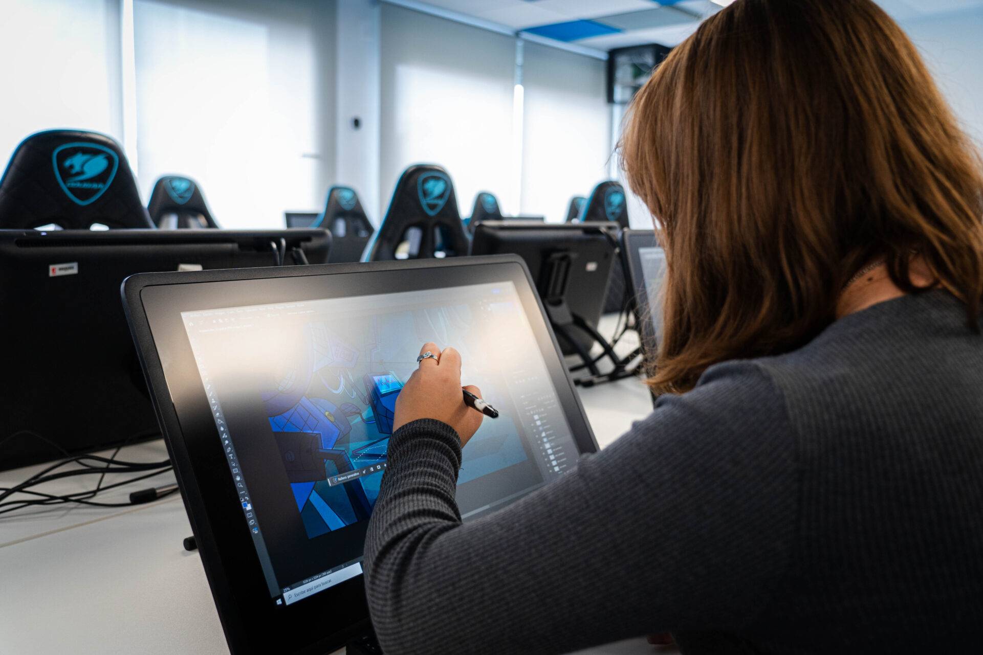 Una persona está dibujando en una tableta gráfica en un aula con pantallas en el fondo.