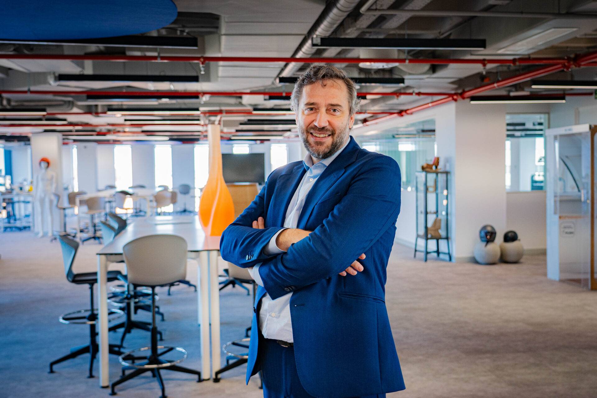 Hombre sonriente de pie en una oficina moderna con un ambiente luminoso y muebles contemporáneos.