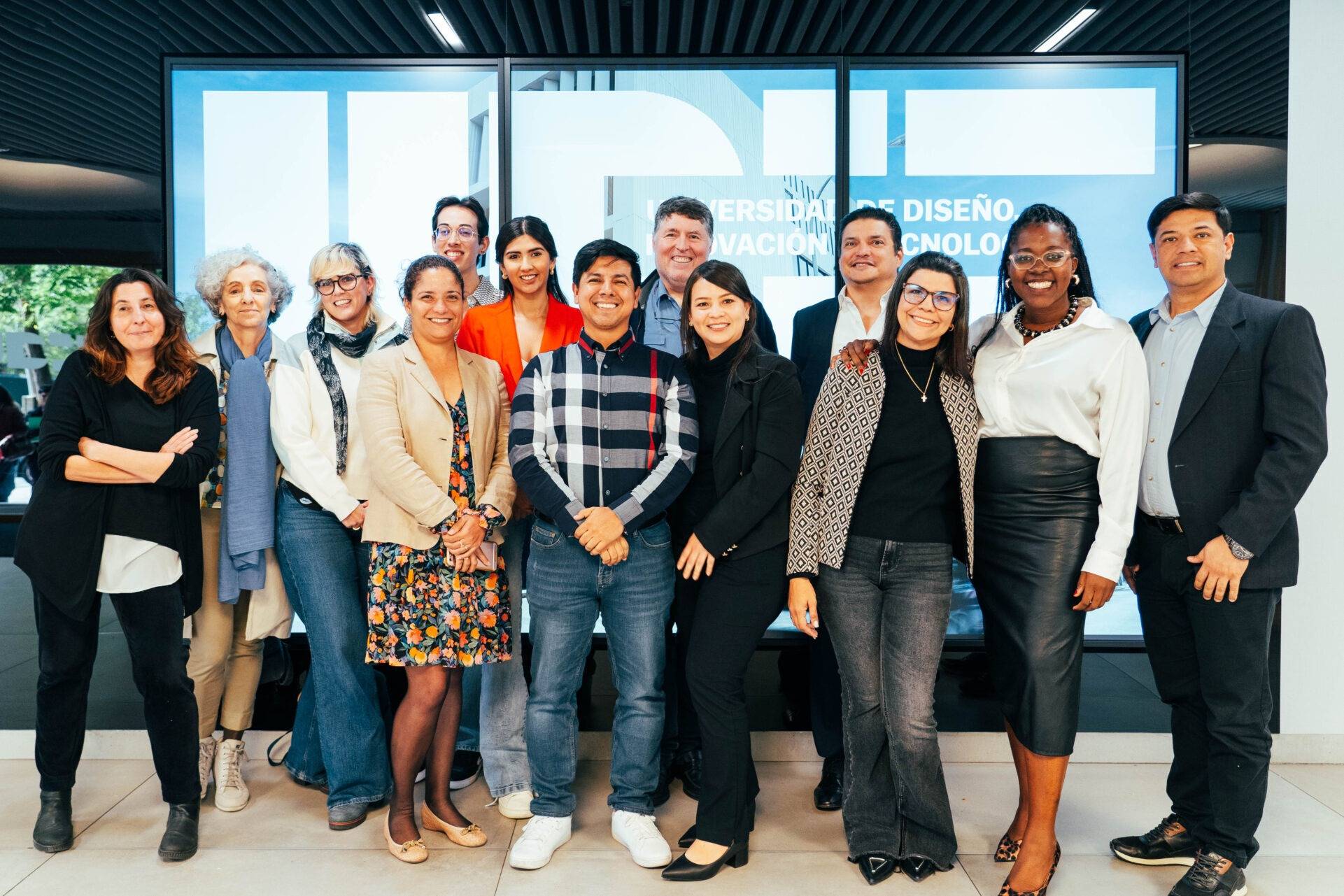 Grupo de personas posando juntas frente a una pantalla en un entorno académico.