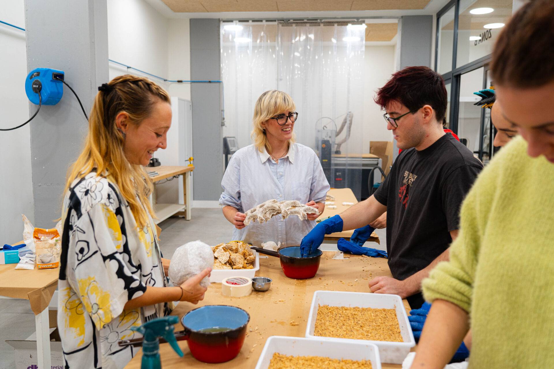 Un grupo de alumnos está trabajando en una mesa, preparando materiales en un ambiente de taller y colaboración.