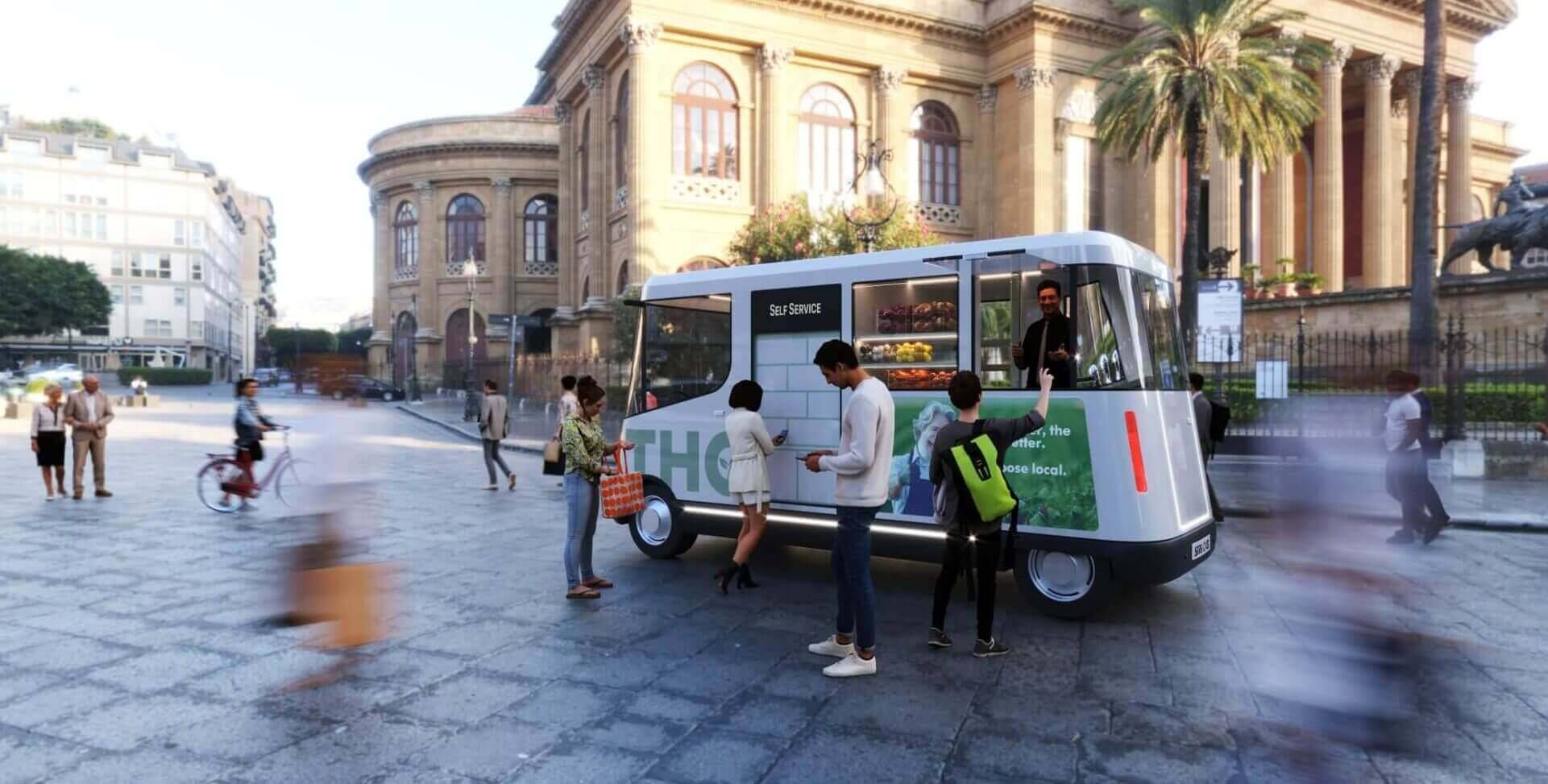 Un food truck moderno está estacionado en una plaza concurrida, con personas caminando y ciclistas alrededor.