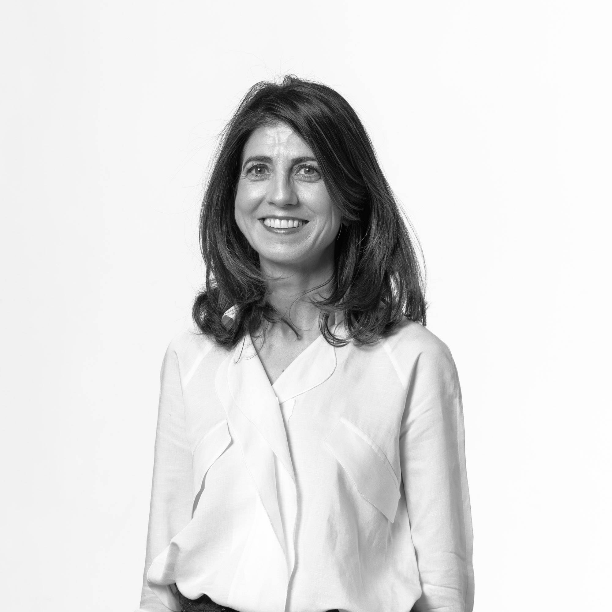 Una mujer sonriente con cabello largo y lacio, vestida con una blusa blanca, frente a un fondo blanco.