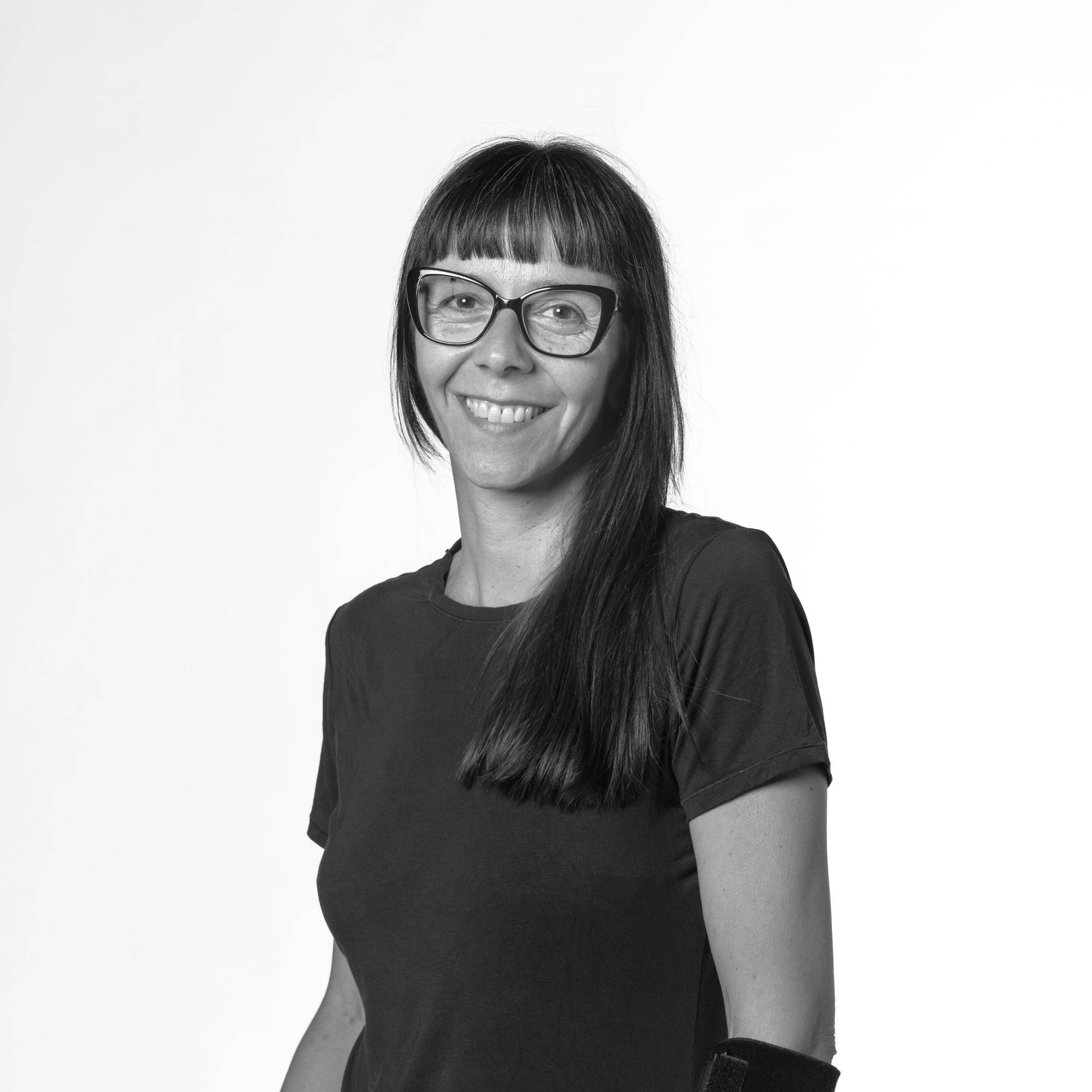Una mujer sonriente con gafas y cabello largo se presenta ante un fondo blanco.