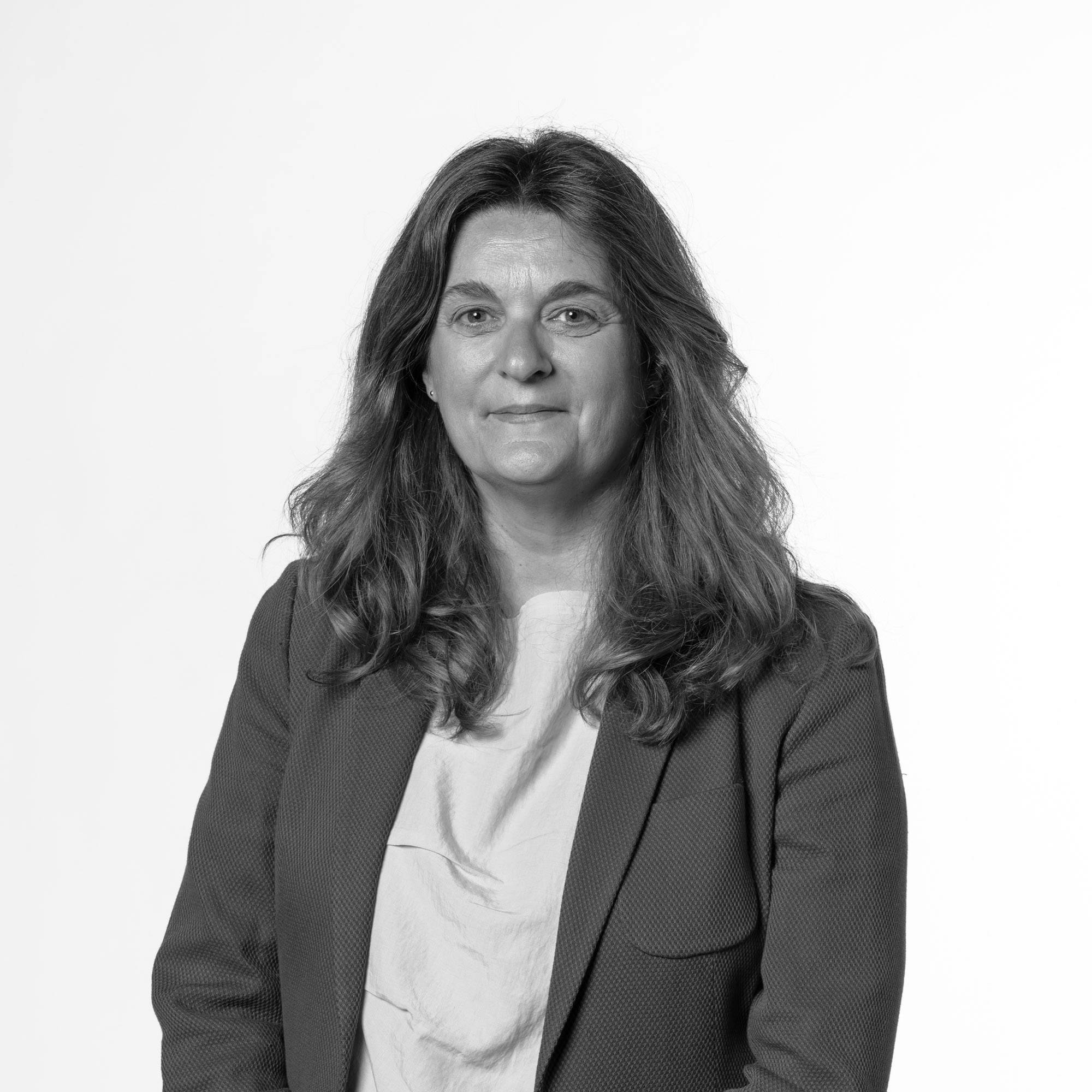 Una mujer sonriente con cabello rizado y blazer en un fondo blanco.