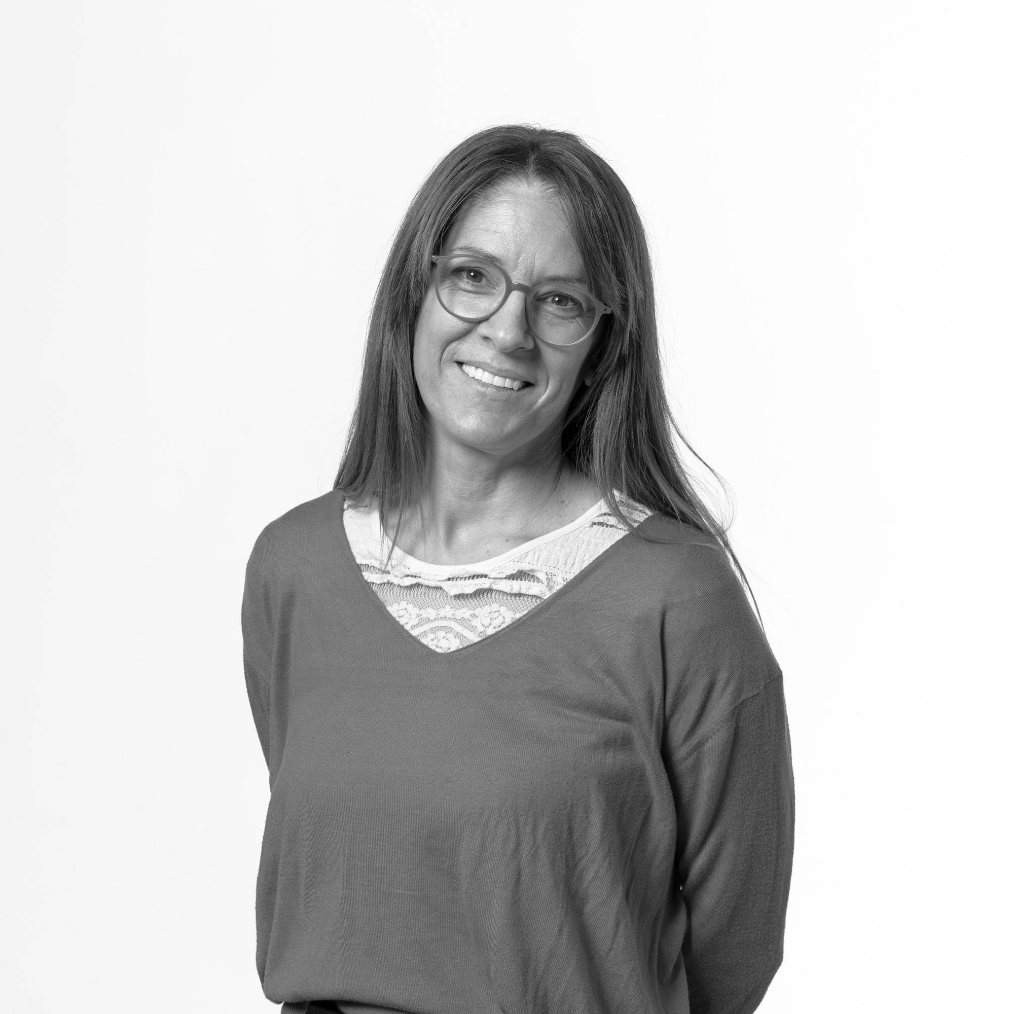 Una mujer sonriente con gafas y cabello largo posa en un fondo blanco.