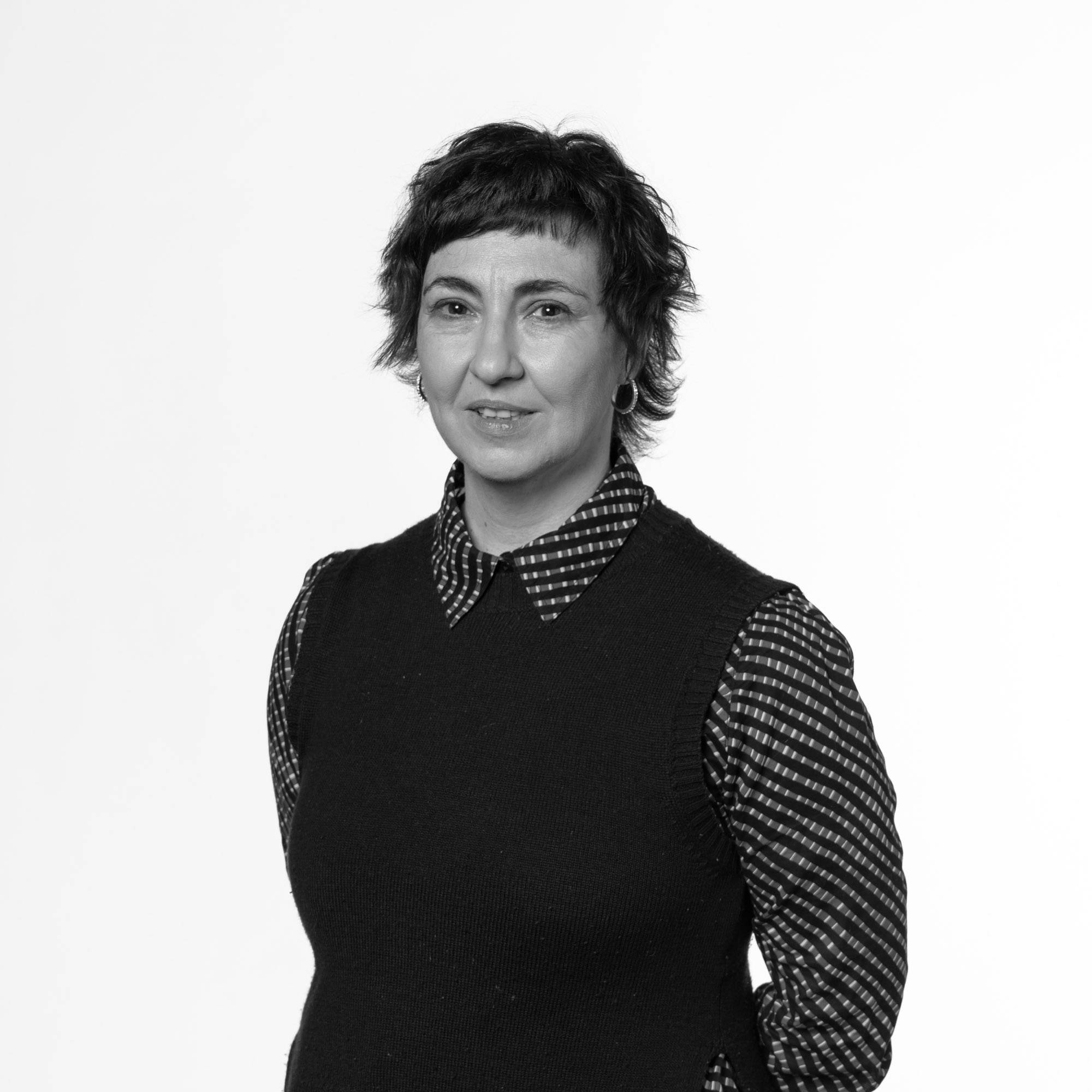Una mujer sonriente con cabello corto y oscuro, vestida con un suéter negro y una camisa de rayas.