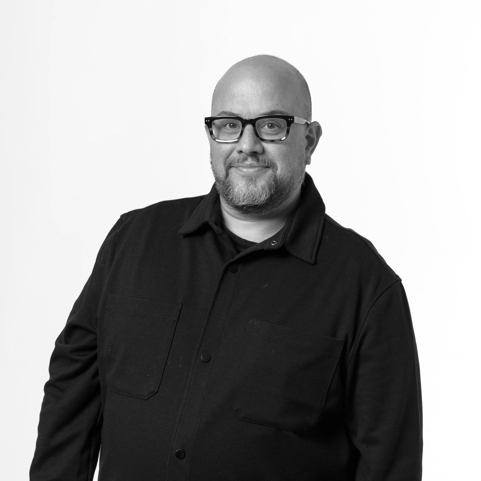 Retrato en blanco y negro de un hombre con gafas y barba, vistiendo una camisa de manga larga.