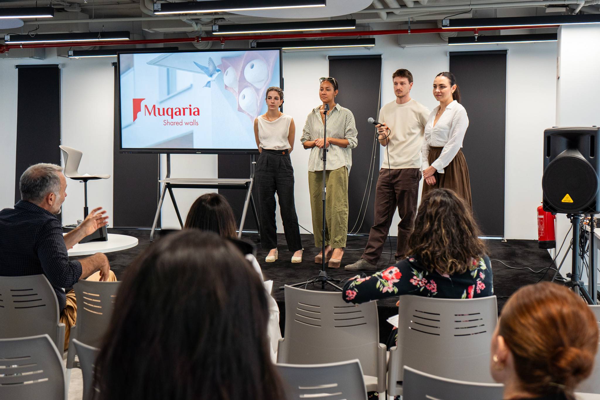 Un grupo de cuatro personas se presenta en un evento frente a una audiencia en un espacio moderno.