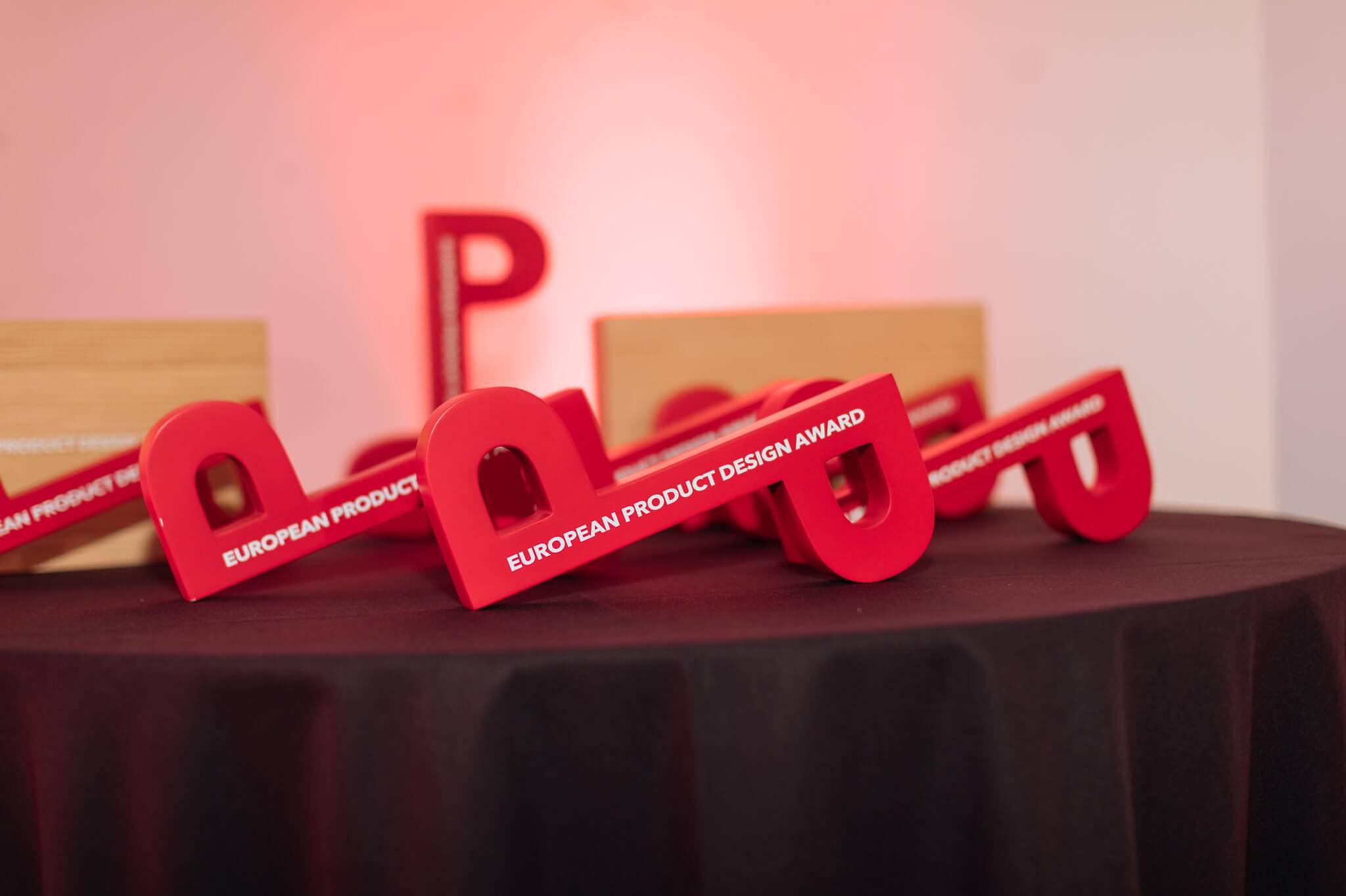 La imagen muestra varios trofeos rojos del European Product Design Award sobre una mesa negra.