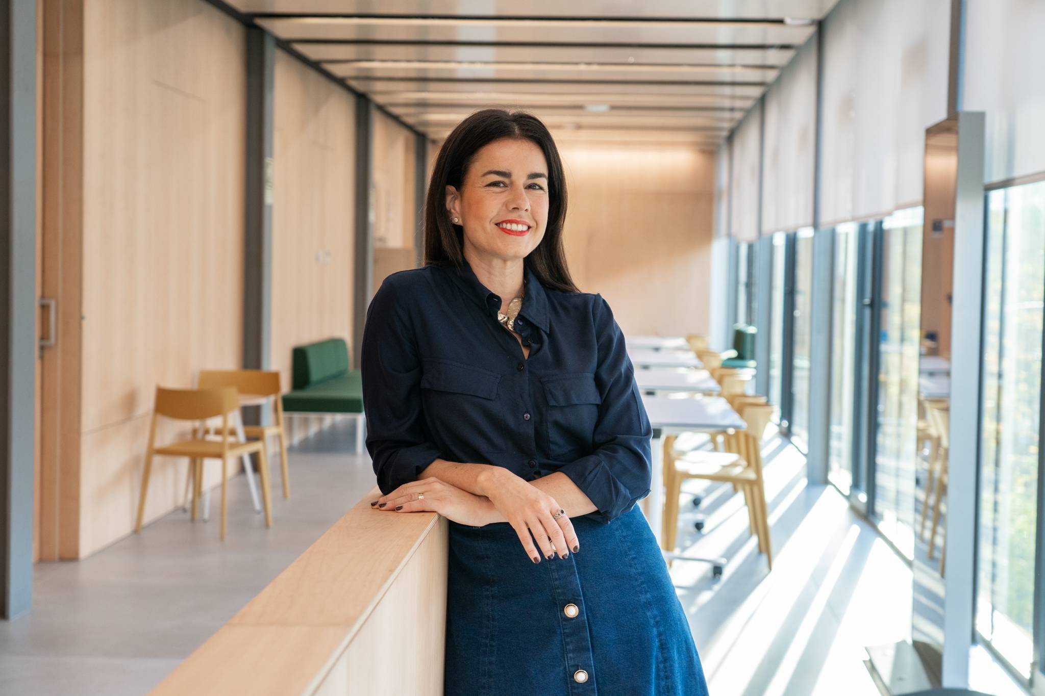 Mujer sonriente de pie junto a una pared de madera en un espacio moderno y luminoso.