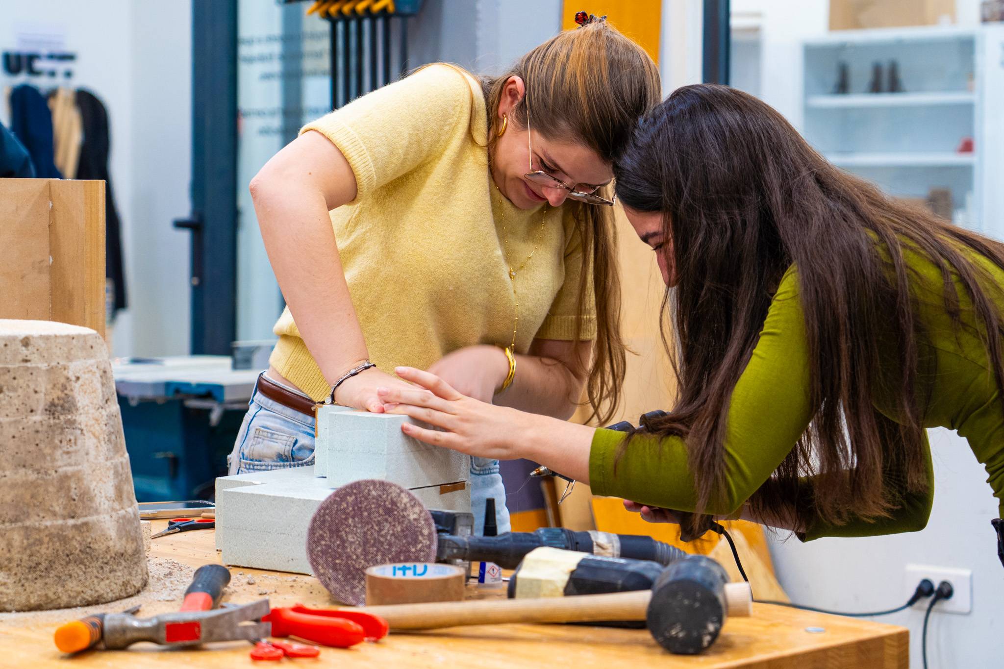 Dos mujeres trabajan juntas en un taller, utilizando herramientas para crear algo.