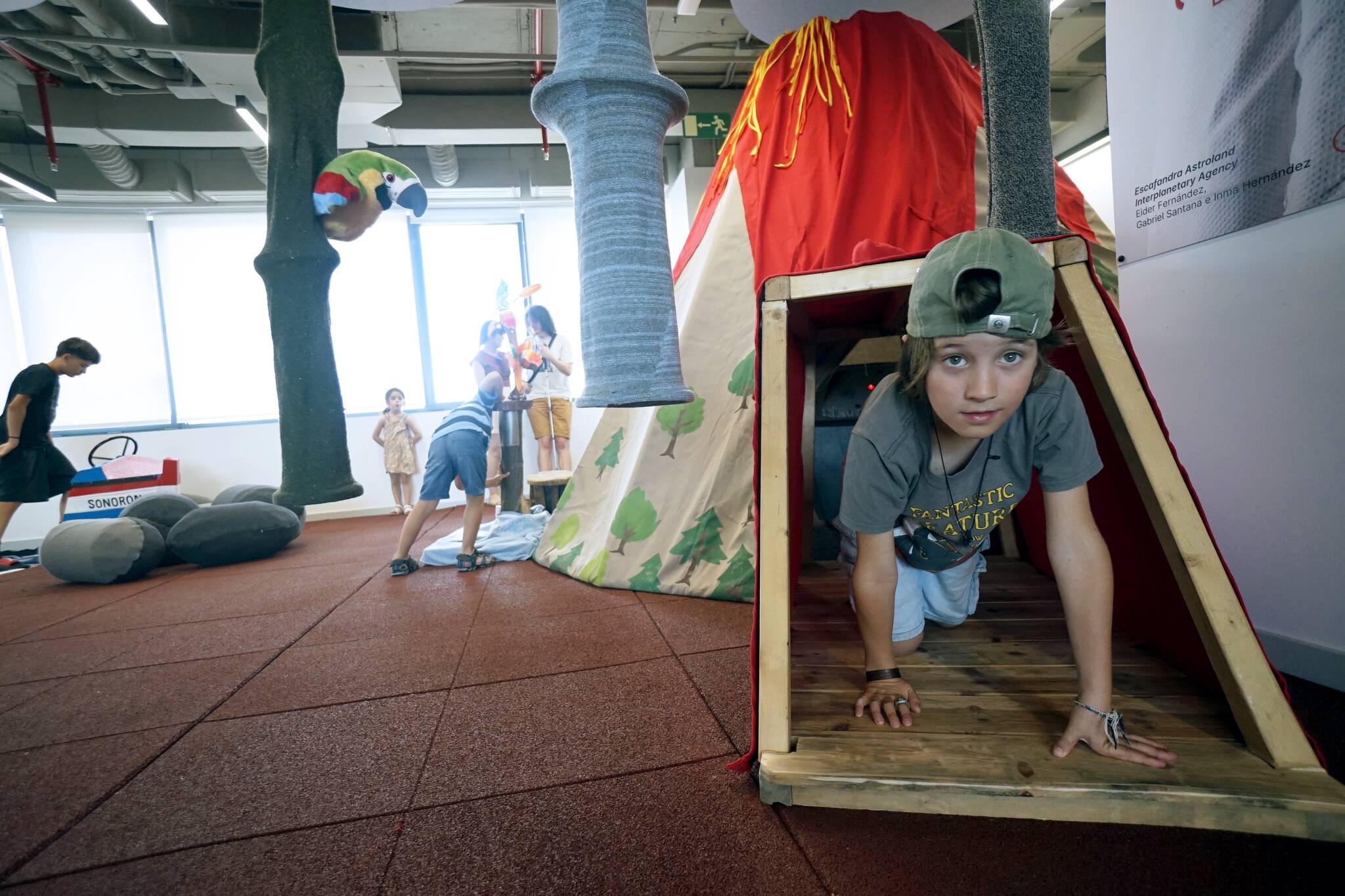 Un grupo de niños juega en un espacio con estructuras de juego y una tienda de campaña en forma de volcán.