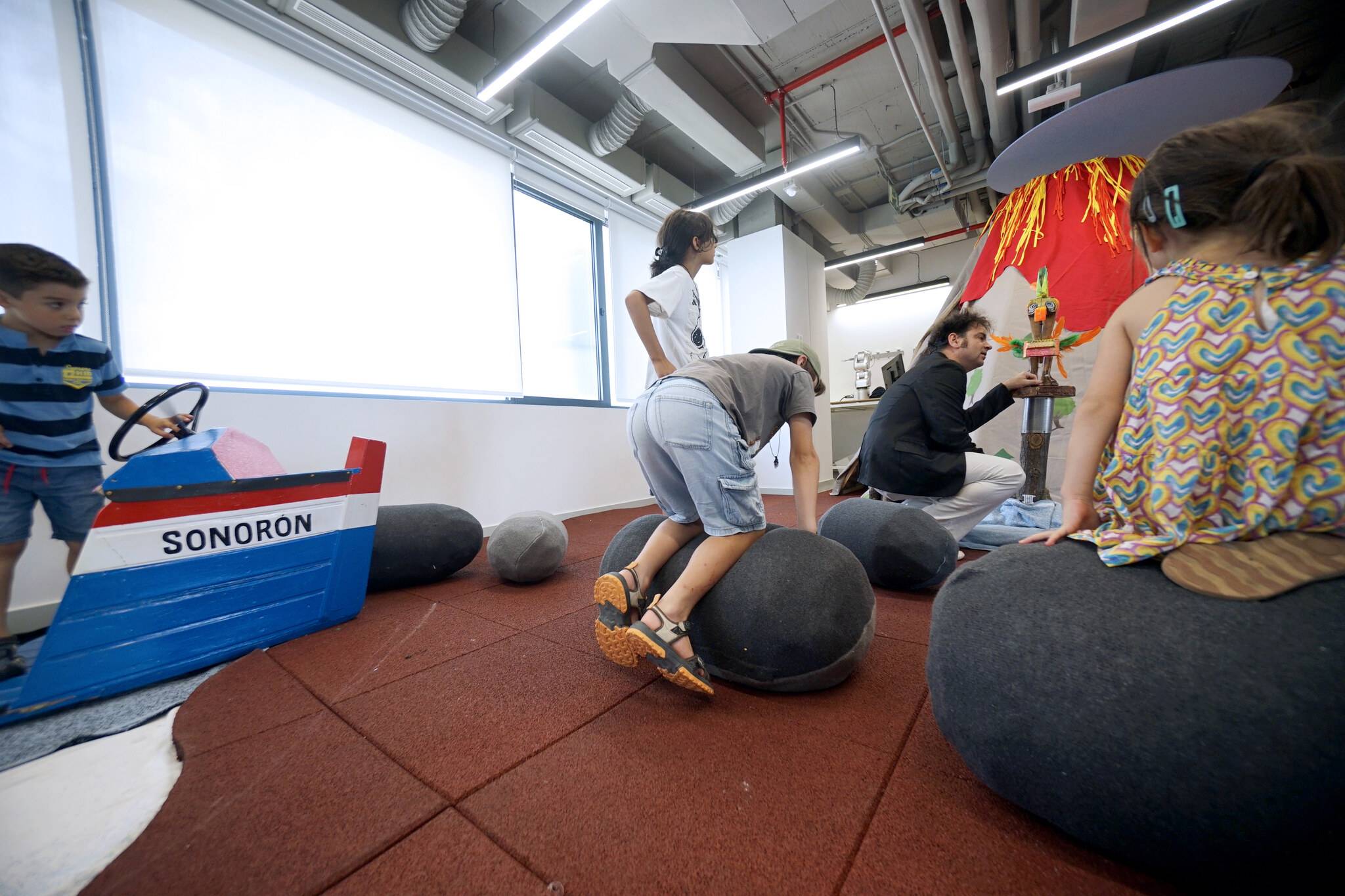 Un grupo de niños juega en un espacio recreativo con elementos de juego y decoraciones coloridas.