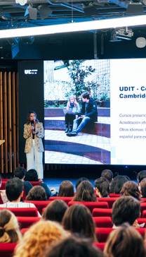 Una conferencia en un auditorio con un presentador frente a una pantalla mostrando información sobre cursos de inglés.