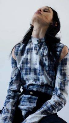 Una modelo con una blusa de cuadros y un peinado moderno se encuentra posando con una actitud sofisticada.