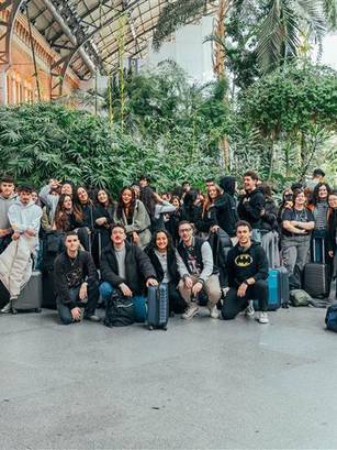 Un grupo de estudiantes posa en una estación con equipaje y plantas alrededor.