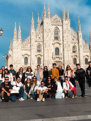 Un grupo grande de personas posa frente a una catedral impresionante en una plaza soleada.