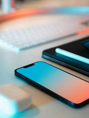 Una imagen que muestra un teléfono, auriculares, un ratón y una tablet sobre una mesa con iluminación tenue.
