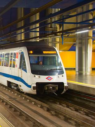 Una estación de metro con un tren llegando y varias personas esperando con maletas.