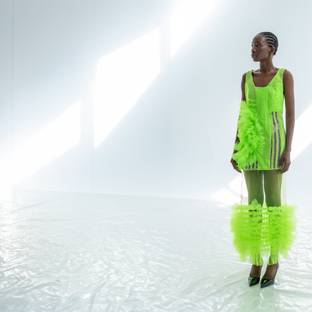 Una modelo viste un traje verde brillante con detalles llamativos en un fondo minimalista.