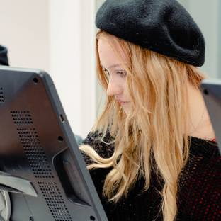 Una joven con sombrero se concentra en la pantalla de una computadora.