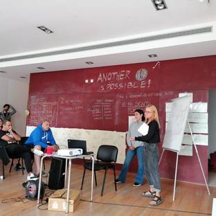 Una reunión en un espacio de trabajo donde dos personas están presentando frente a un grupo de asistentes.