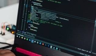 Una persona está programando en un ordenador portátil con código visible en la pantalla.