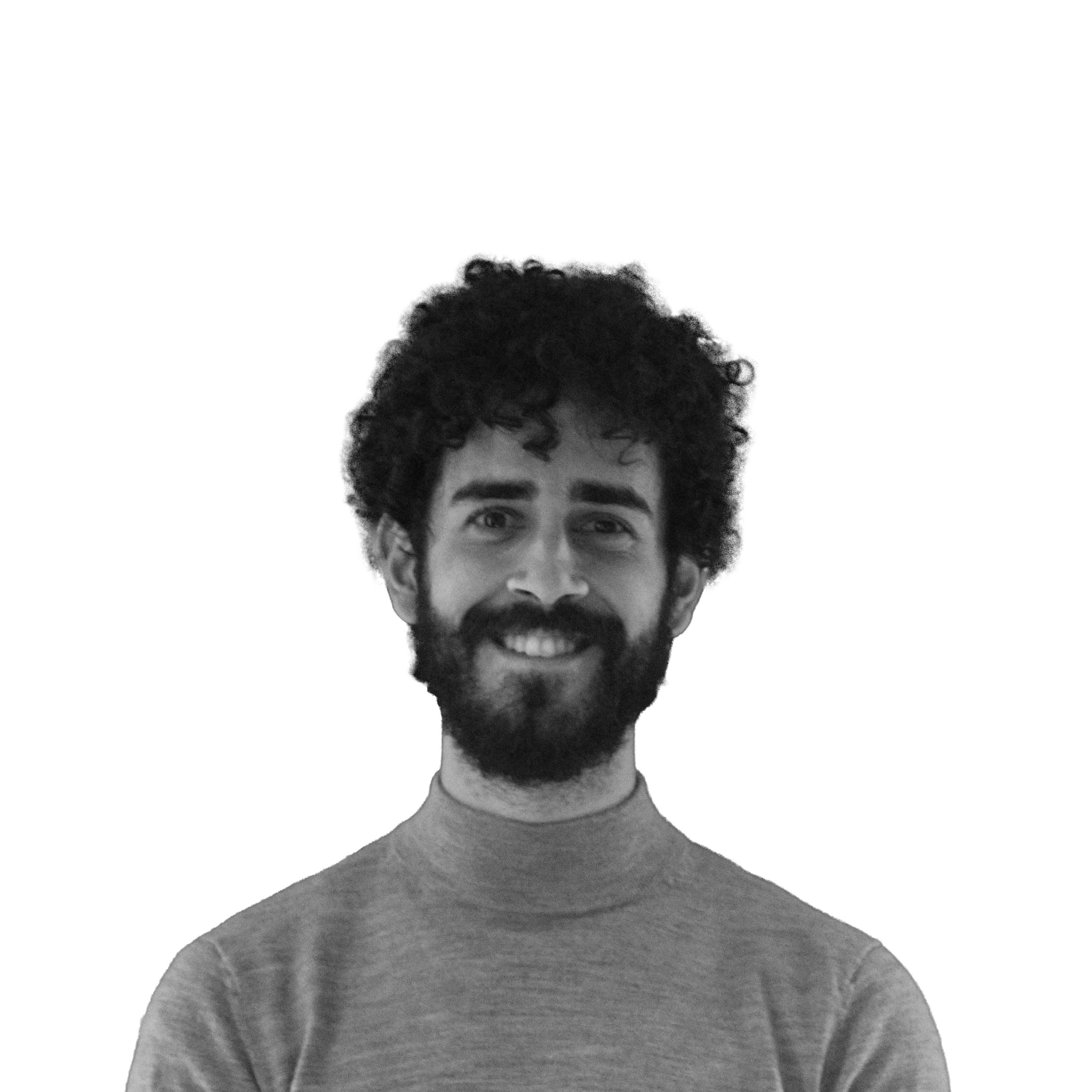 Un hombre con cabello rizado y barba sonríe frente a un fondo blanco.