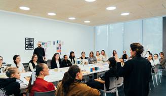 Un grupo de personas asiste a una clase o taller, prestando atención a un presentador en un aula iluminada.
